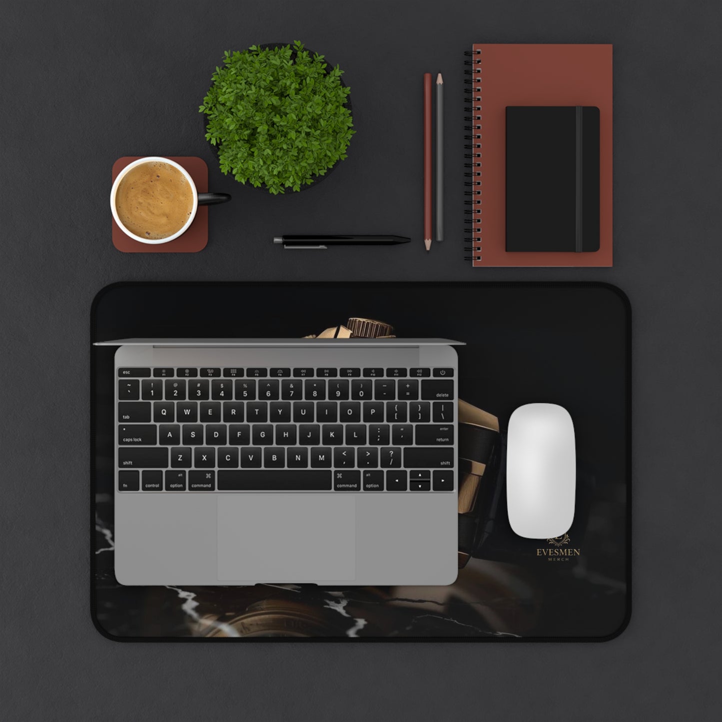 Laptop on a desk with a coffee cup, plant, notebook, and mouse. Underneath it is a mouse pad.