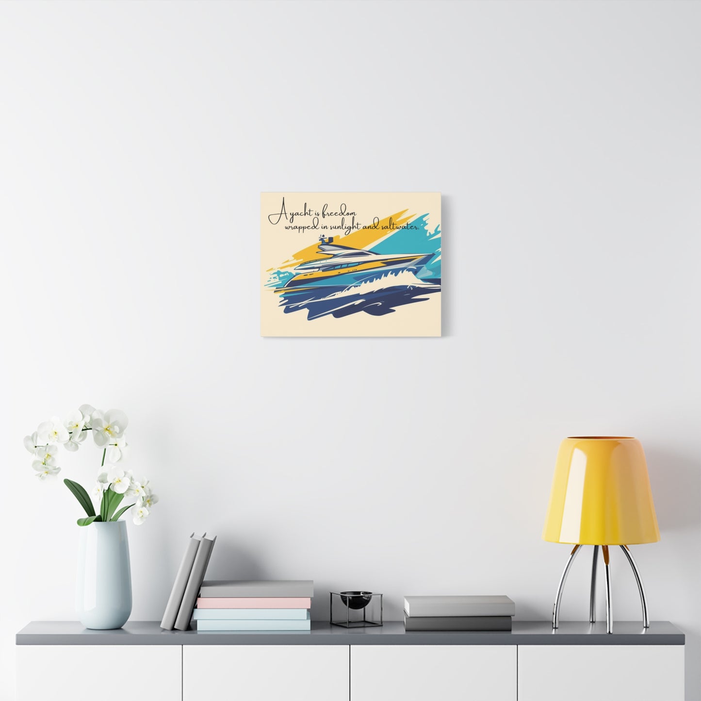 Decorative wall art with abstract design and text on a white wall above a shelf with books and a lamp.