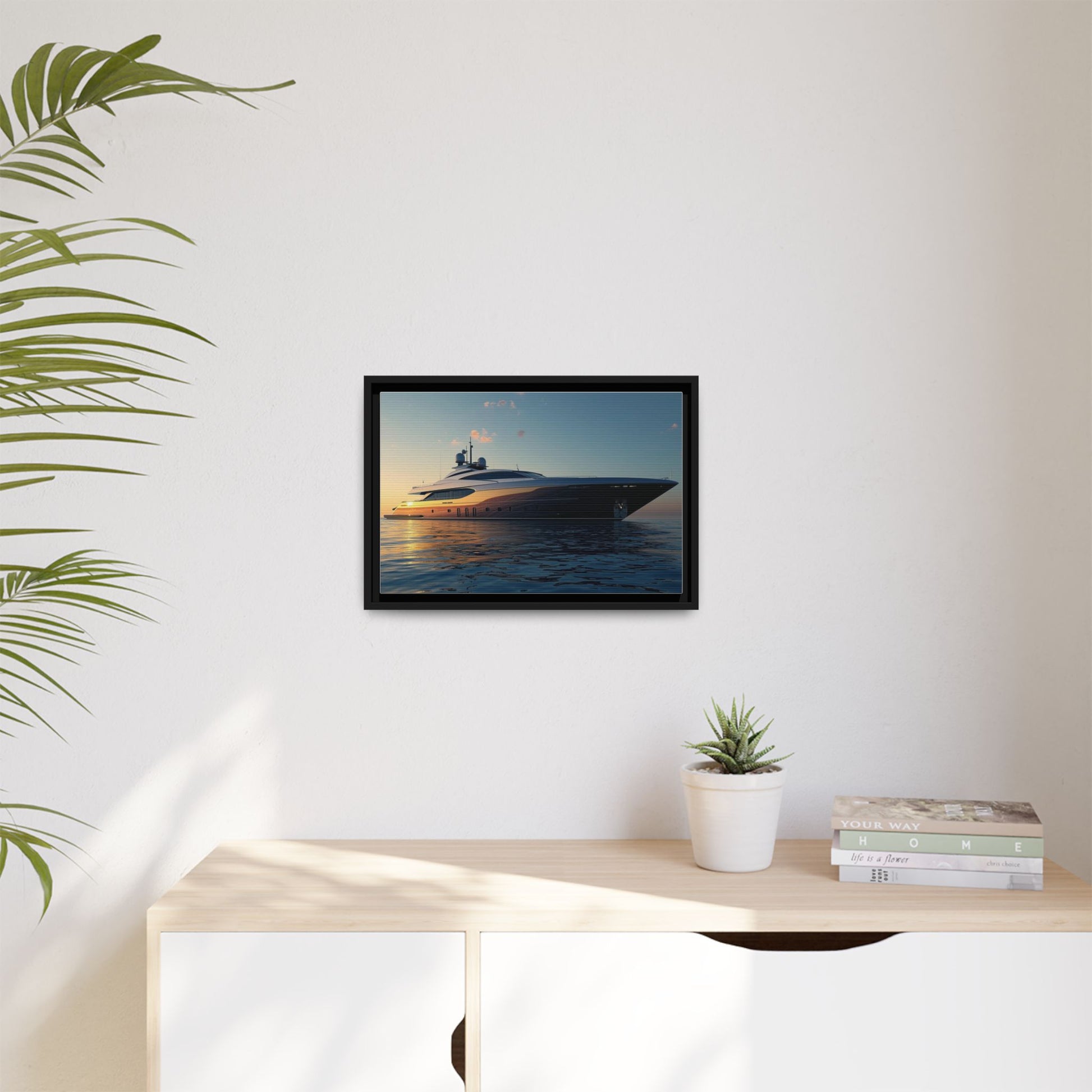 Framed artwork of a yacht on a wall above a desk with a plant and books.