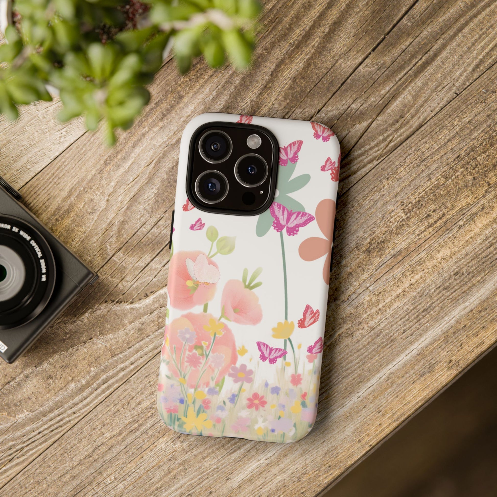 Floral phone case on a wooden surface with a camera and plant in the background