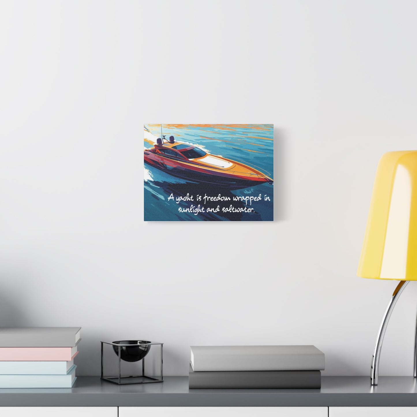 Canvas wall art of a yacht on a wall above a desk with books and a lamp.