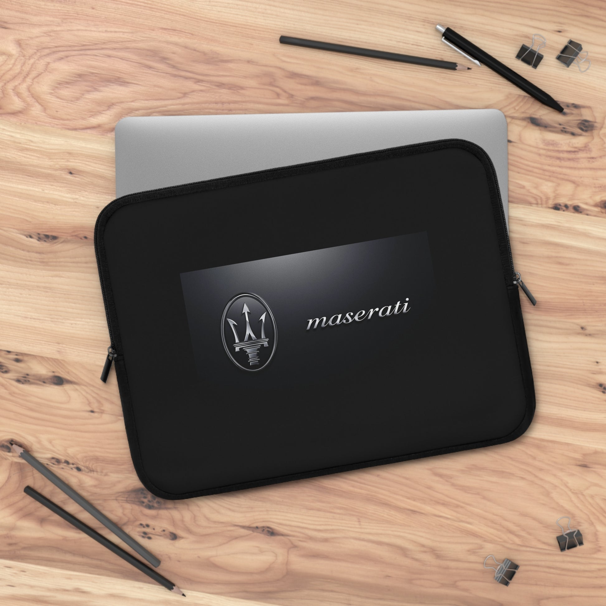 Black Maserati laptop sleeve on a wooden surface with pencils and stationery.
