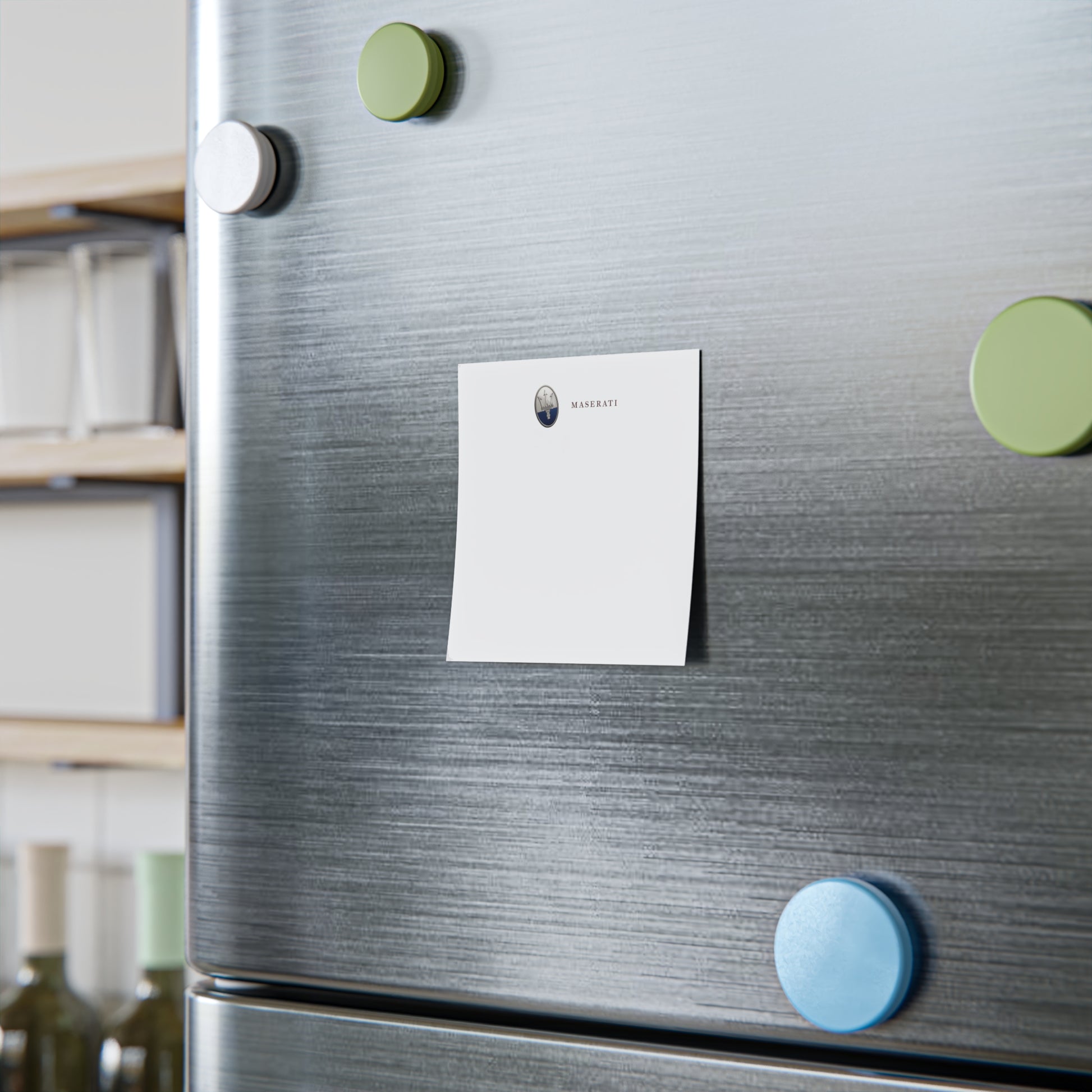 Silver refrigerator with a white magnet and green and blue circular magnets on a kitchen background