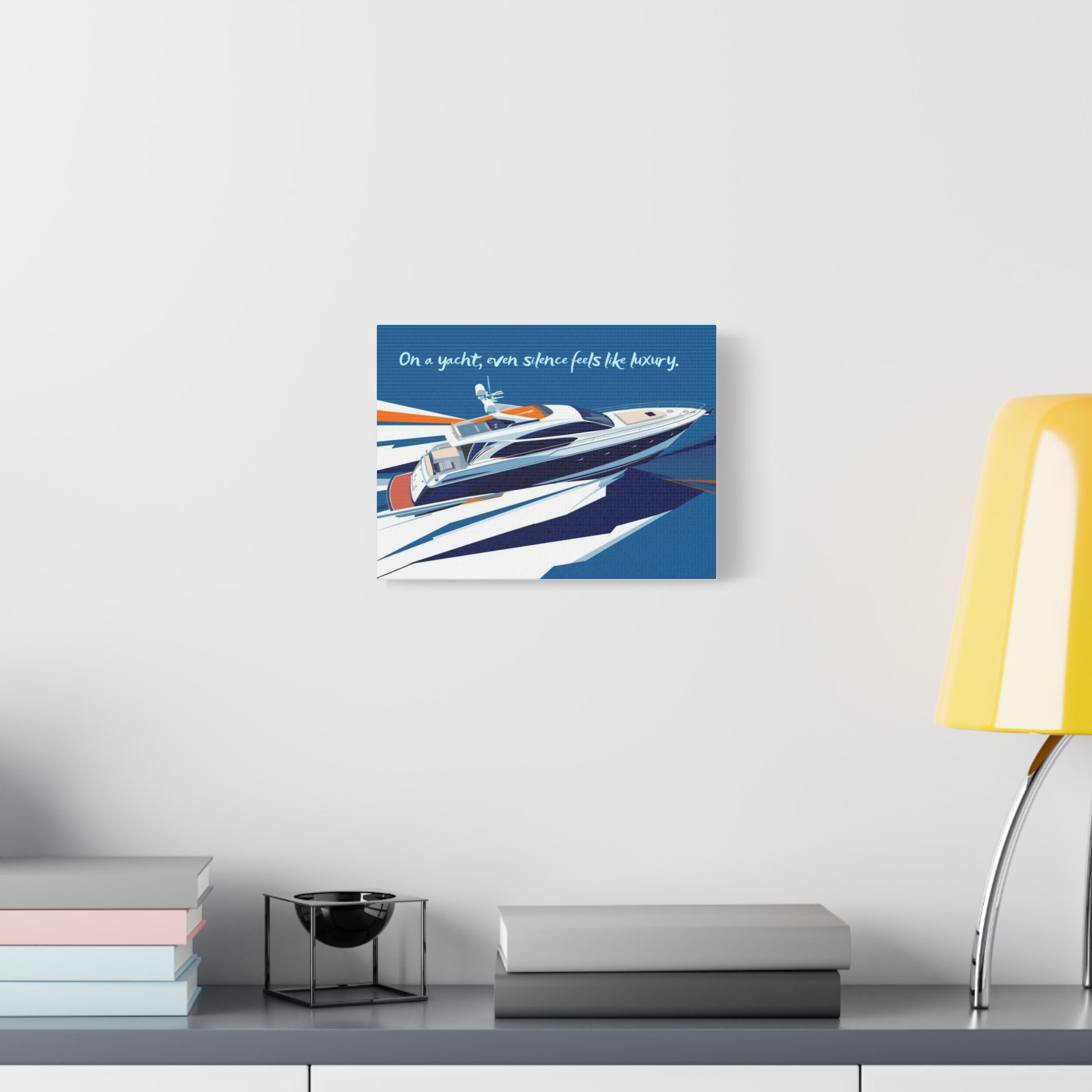 Framed artwork of a yacht on a white wall above a desk with books and a lamp.