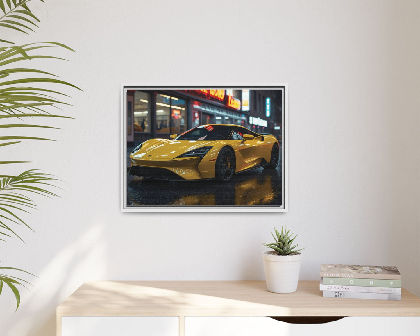 White framed Yellow sports car in a framed picture on a wall above a desk with a plant and books.
