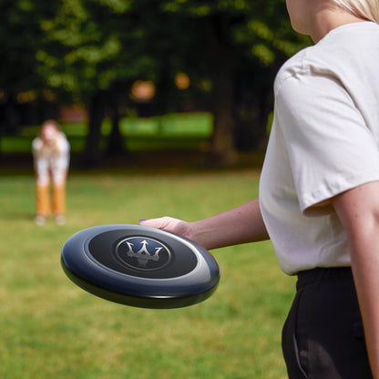 Person holding a black and gray frisbee with a logo in a park setting