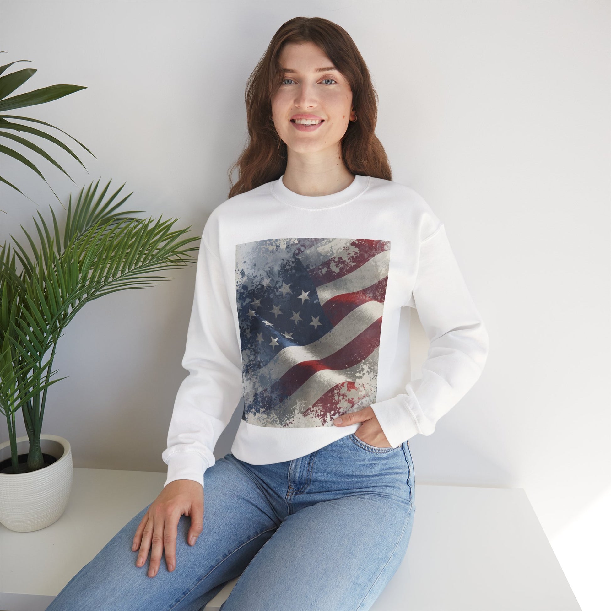 Woman wearing a white sweatshirt with a vintage American flag design, sitting in a room with a plant.