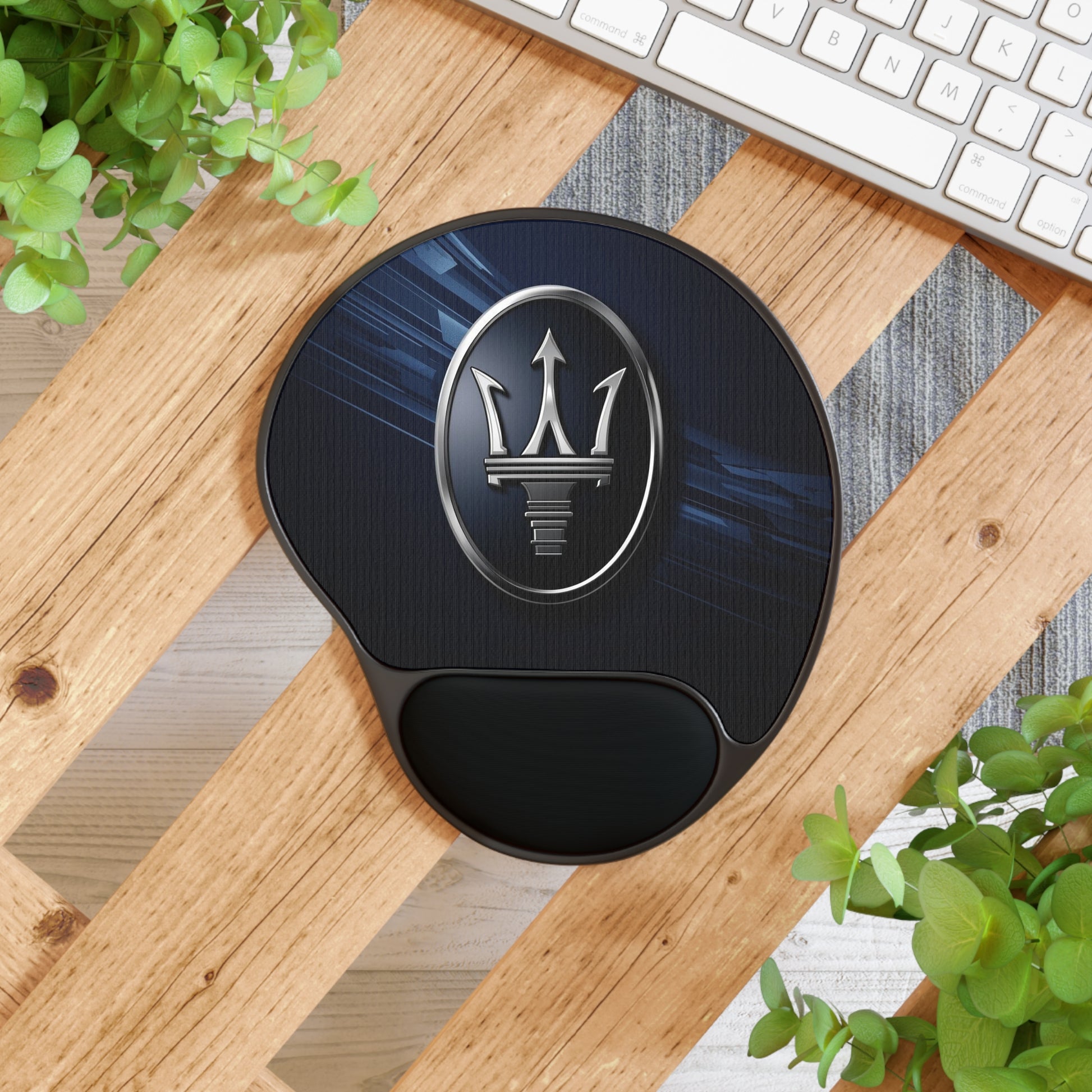 Black wrist rest with Maserati logo on a wooden desk with plants and a keyboard.
