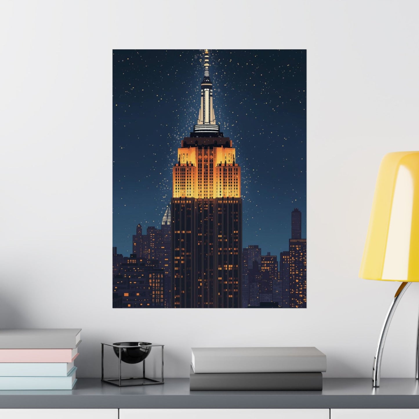 Framed artwork of the Empire State Building on a wall above a desk with books and a lamp.