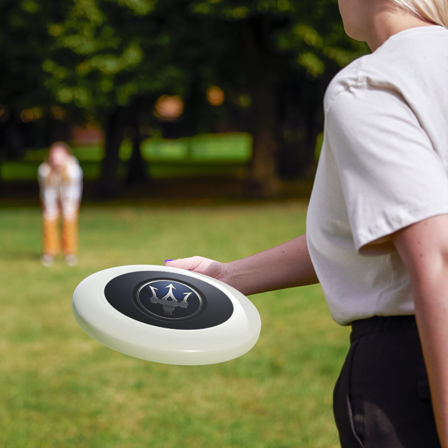 Person holding a frisbee with a logo in a park setting