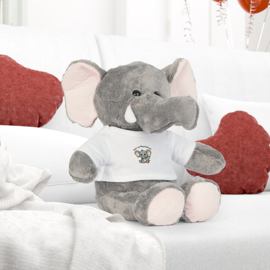 Gray stuffed plushie elephant toy with a white shirt on a bed with red heart pillows