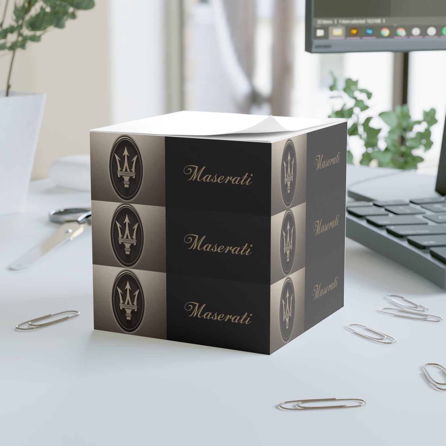 Maserati logo on the sides of a note cube with paper clips around the the cube and a computer on the side