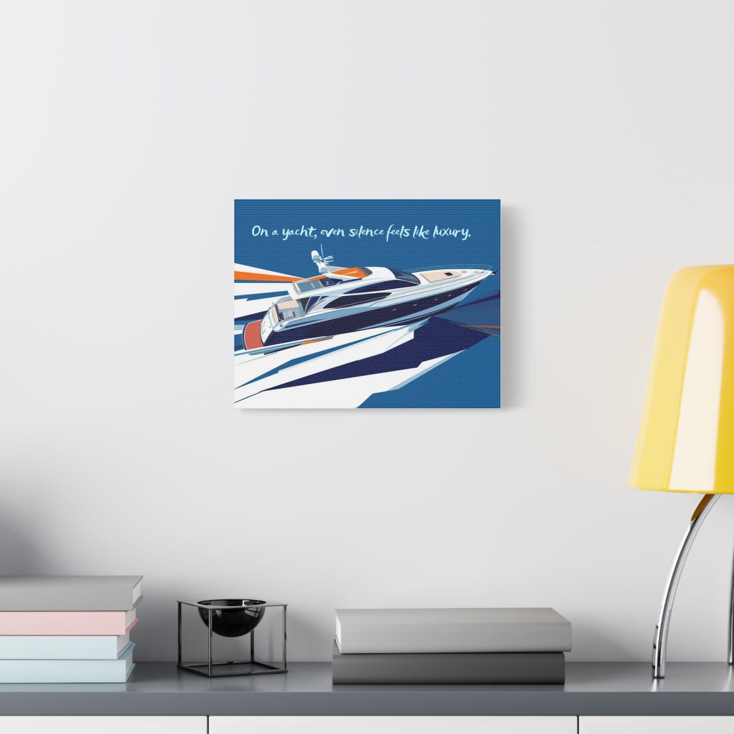 Yacht illustration wall art with a blue background in a white wall above a desk with books and a lamp.