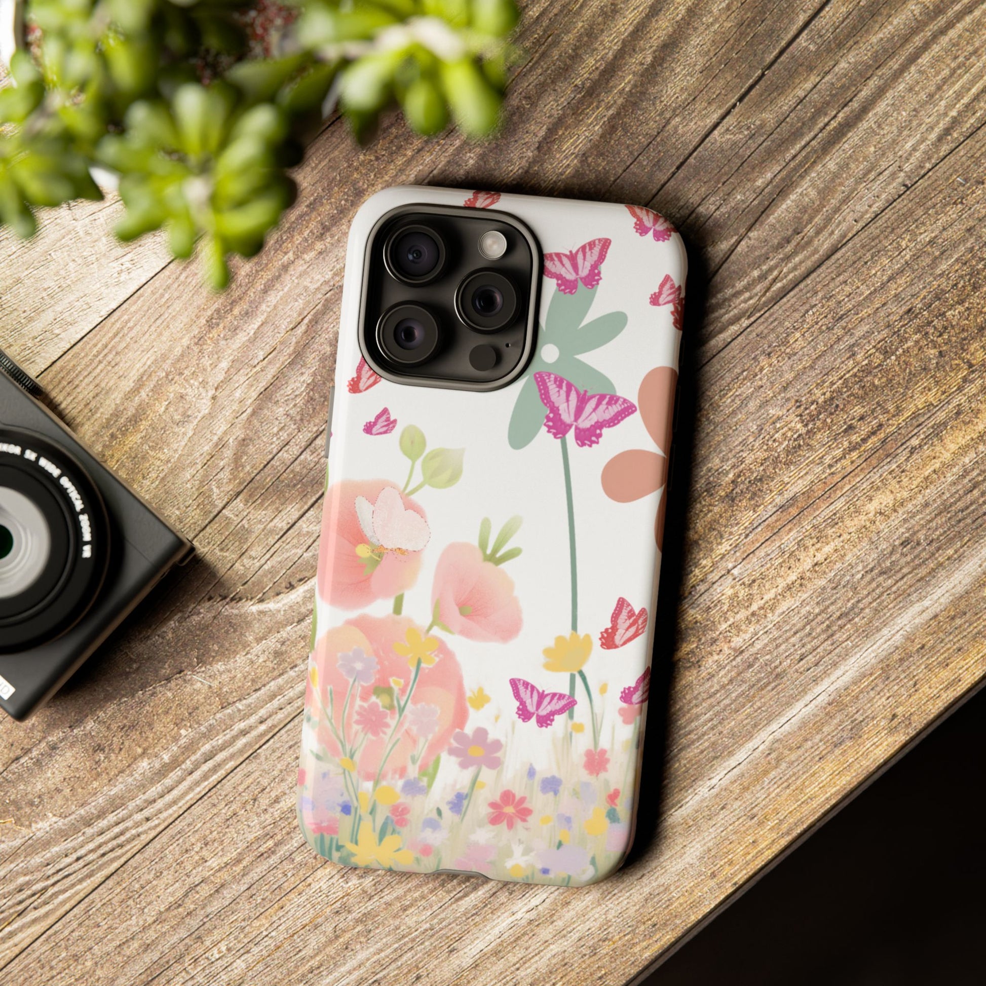 Floral phone case on a wooden surface with a camera and plant in the background