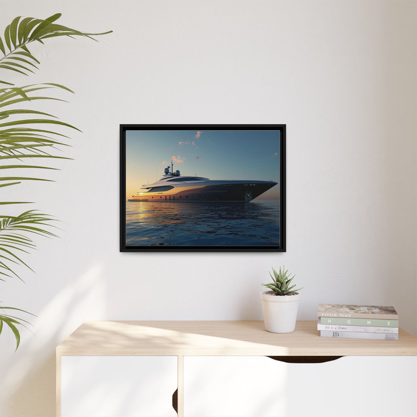 Framed artwork of a yacht on a wall above a desk with a plant and books.