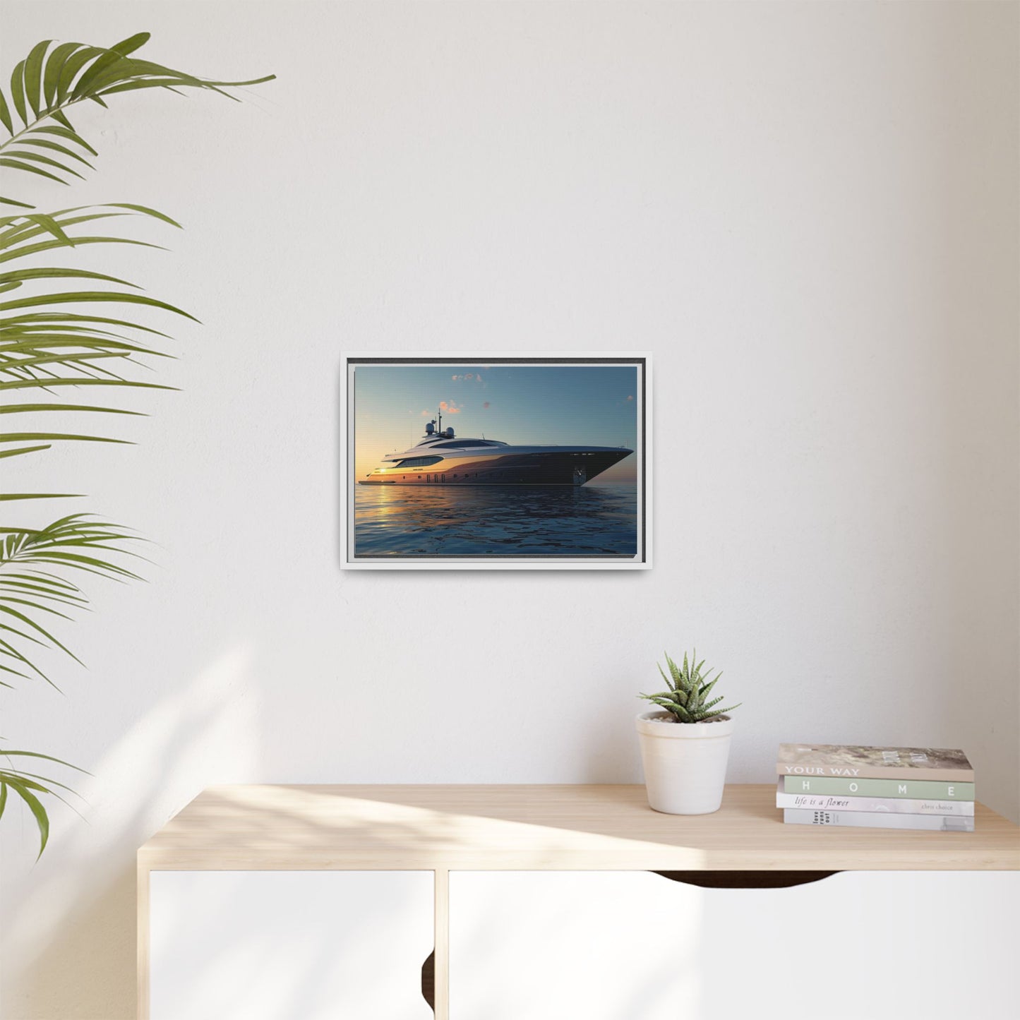 Framed artwork of a yacht on a wall above a desk with a plant and books.