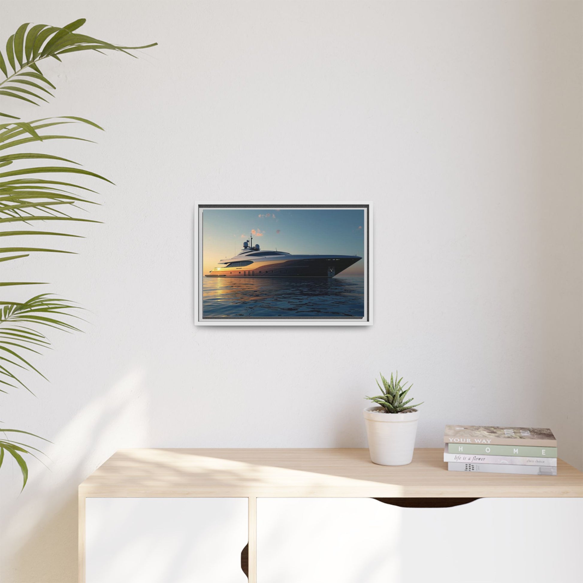 Framed artwork of a yacht on a wall above a desk with a plant and books.