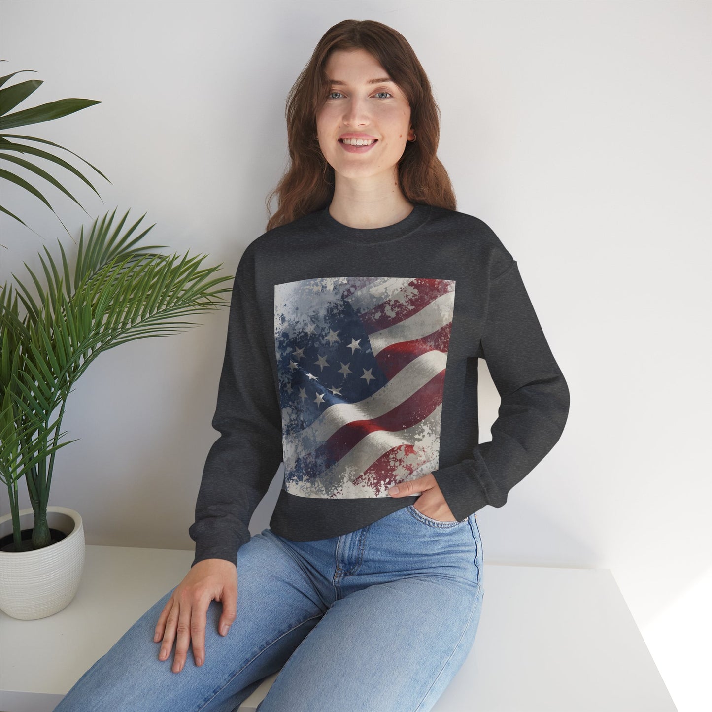 Woman wearing a black sweatshirt with a vintage American flag design, sitting on a white surface with a plant in the background.