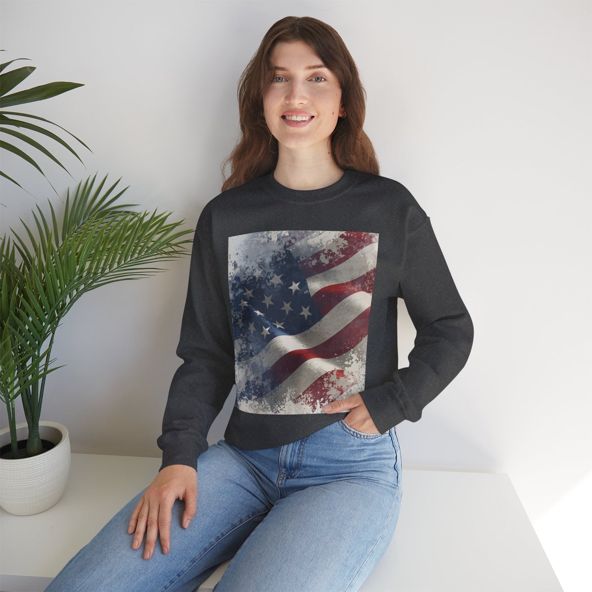 Woman wearing a black sweatshirt with a vintage American flag design, sitting on a white surface with a plant in the background.