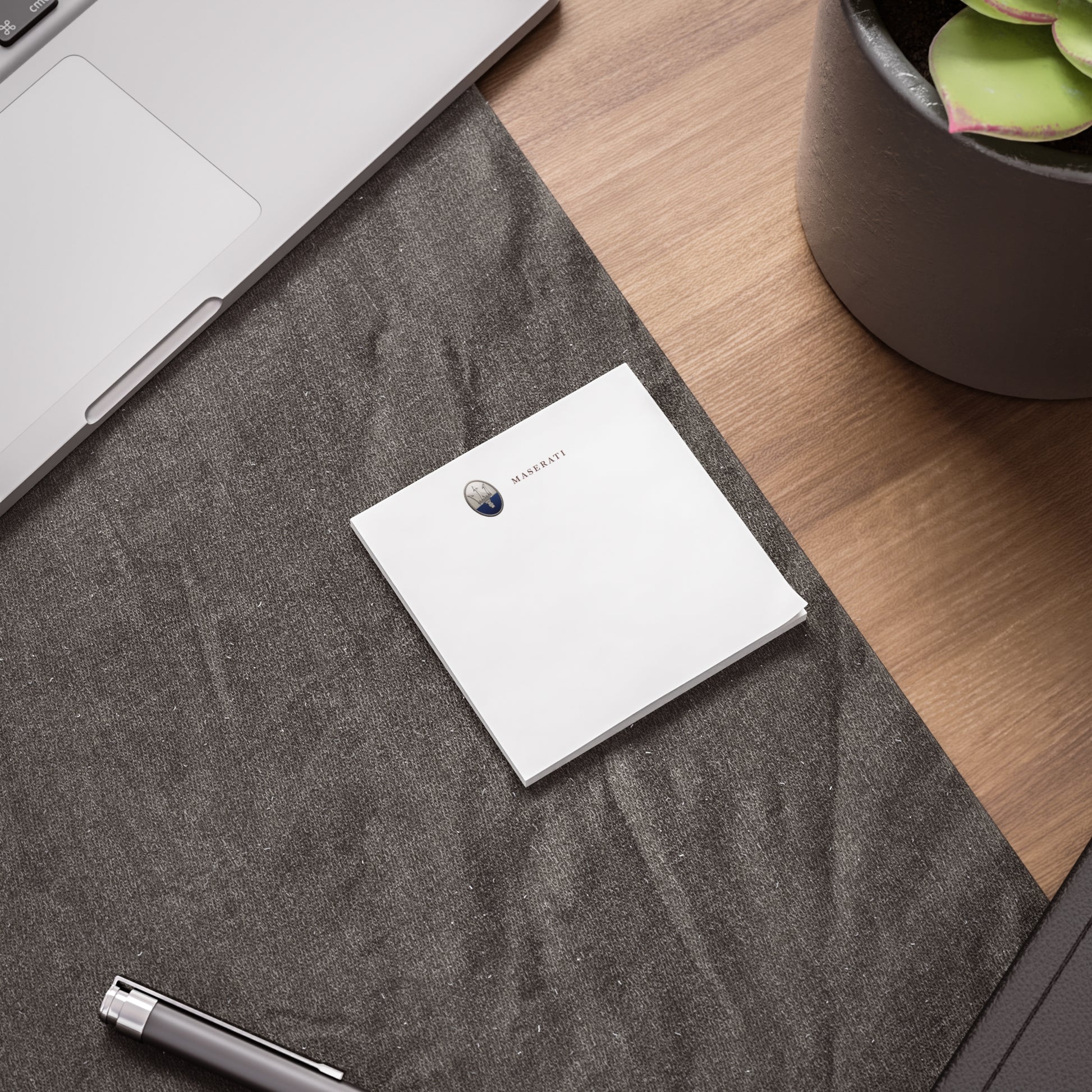 White notebook on a textured gray surface with a laptop and plant in the background
